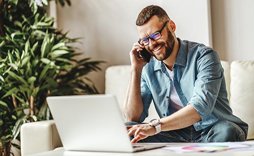 man on cell phone and laptop smiling