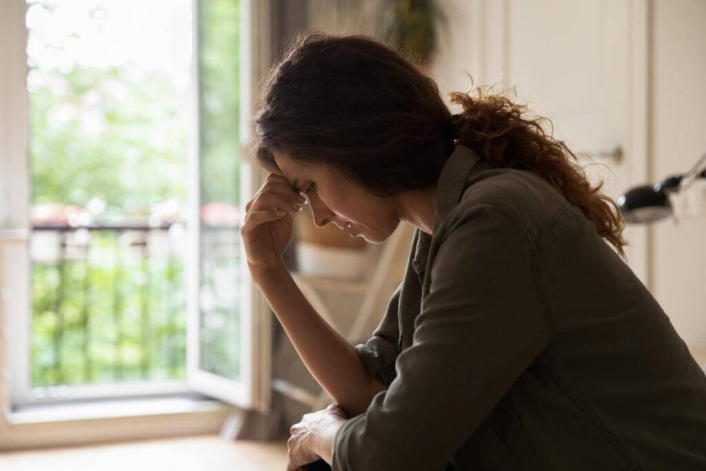 Depressed woman with her hand pressed against her forehead experiencing dual diagnosis symptoms